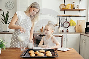 Cute little girl and mom eating freshly baked cookies with milk