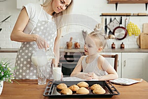 Cute little girl and mom eating freshly baked cookies with milk