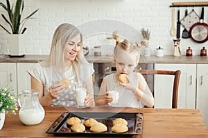 Cute little girl and mom eating freshly baked cookies with milk