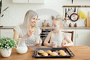 Cute little girl and mom eating freshly baked cookies with milk