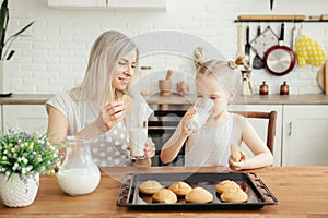 Cute little girl and mom eating freshly baked cookies with milk