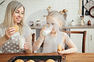 Cute little girl and mom eating freshly baked cookies with milk