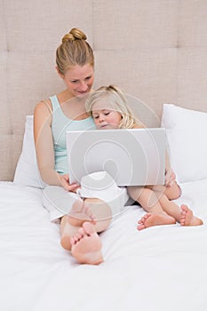 Cute little girl and mother on bed using laptop