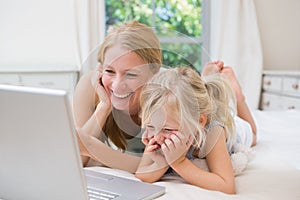 Lindo pequeno a madre sobre el una cama computadora portátil 