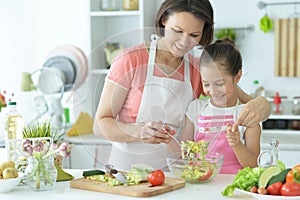 Cute little girl with mother cooking together at kitchen table