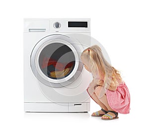 Cute little girl near washing machine with laundry