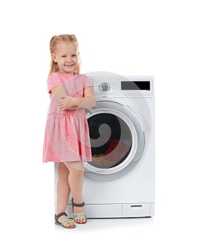 Cute little girl near washing machine with laundry