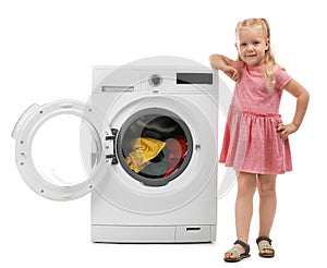 Cute little girl near washing machine with laundry