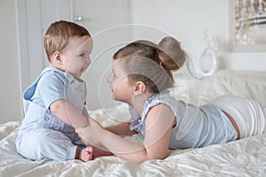 Cute little girl older sister with her baby boy brother at home lying on bed