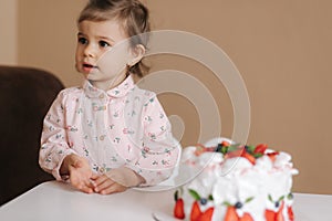 Cute little girl one and a hulf year old stand by delicious birthday cake. Eighteen month old girl verry happy and