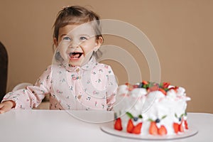 Cute little girl one and a hulf year old stand by delicious birthday cake. Eighteen month old girl verry happy and