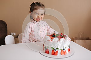 Cute little girl one and a hulf year old stand by delicious birthday cake. Eighteen month old girl verry happy and