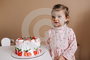 Cute little girl one and a hulf year old stand by delicious birthday cake. Eighteen month old girl verry happy and