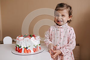 Cute little girl one and a hulf year old stand by delicious birthday cake. Eighteen month old girl verry happy and