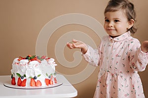 Cute little girl one and a hulf year old stand by delicious birthday cake. Eighteen month old girl verry happy and