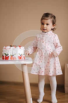 Cute little girl one and a hulf year old stand by delicious birthday cake. Eighteen month old girl verry happy and
