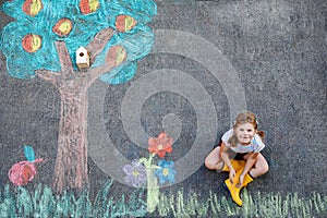 Cute little girl painting with colorful chalks apples harvest from apple tree on asphalt. Cute preschool child with