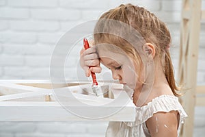 Cute little girl painting wooden rack at home.