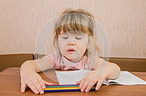 Cute little girl paints and tinkers with colored pencils and scissors