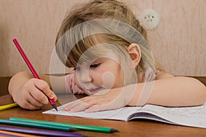 Cute little girl paints and tinkers with colored pencils and scissors