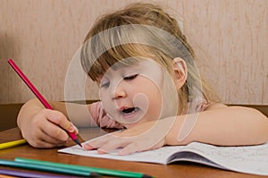 Cute little girl paints and tinkers with colored pencils and scissors