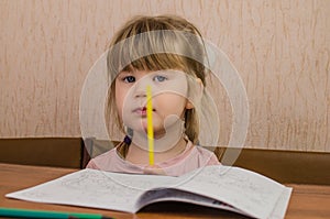 Cute little girl paints and tinkers with colored pencils and scissors