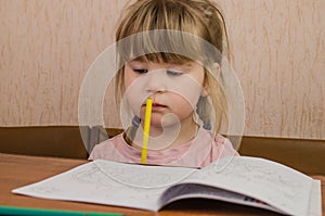 Cute little girl paints and tinkers with colored pencils and scissors