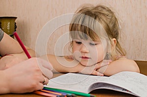 Cute little girl paints and tinkers with colored pencils and scissors