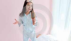 Cute little girl in pajama on the bed holding a hair brush like microphone singing imitates herself a real singer in the morning