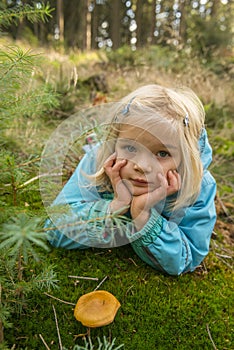 Cute little girl picking mushrooms in summer forest