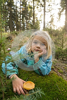 Cute little girl picking mushrooms in summer forest