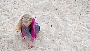 Cute little girl picking pebble stones in dune sand