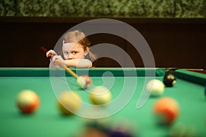 Cute little girl with pigtails playing pool in the