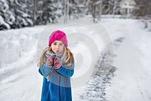 Cute little girl in a pink hat and blue coat freezing in winter