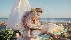 Cute little girl in pink heart sunglasses sitting on mothers laps reading book