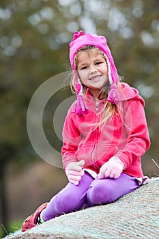 Cute little girl in pink sitting on hay bale.