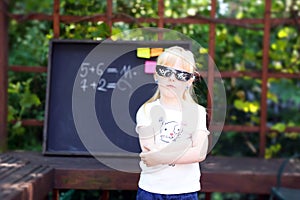 Cute little girl with pixel glasses standing ahead blackboard