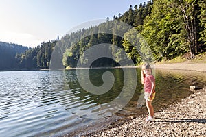 A cute little girl plaing on the bank of a mountain lake on a wa