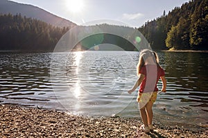 A cute little girl plaing on the bank of a mountain lake on a wa