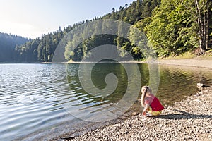 A cute little girl plaing on the bank of a mountain lake on a wa