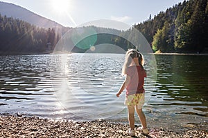 A cute little girl plaing on the bank of a mountain lake on a wa