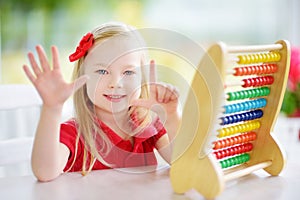 Cute little girl playing with abacus at home. Smart child learning to count.