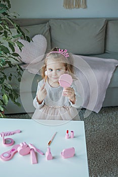 Cute little girl is playing in a beauty salon. Beautiful girl of 3 years old makes makeup with children`s cosmetics at home