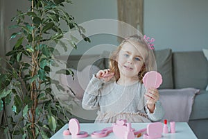 Cute little girl is playing in a beauty salon. Beautiful girl of 3 years old makes makeup with children`s cosmetics at home