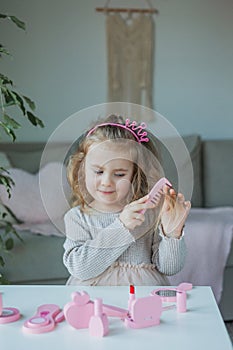 Cute little girl is playing in a beauty salon. Beautiful girl of 3 years old makes makeup with children`s cosmetics at home