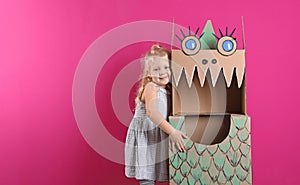 Cute little girl playing with cardboard dragon on color background.