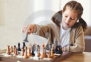 Cute little girl playing chess while spending leisure time at home during during day time