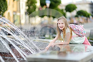 Cute little girl playing by city fountain on hot and sunny summer day. Child having fun with water in summer.