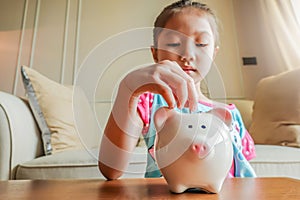 Cute little girl playing collect money with a pink saving Pig Jar