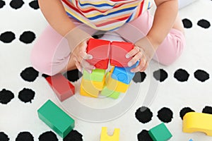 Cute little girl playing with colorful cubes on floor indoors, above view. Educational toy